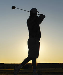 Silhouette of man golfing at sunset